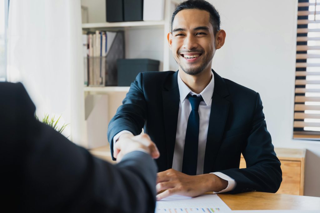 pexels-photo-12885861-12885861 Confident businessman in suit shaking hands at office desk, symbolizing successful partnership.
